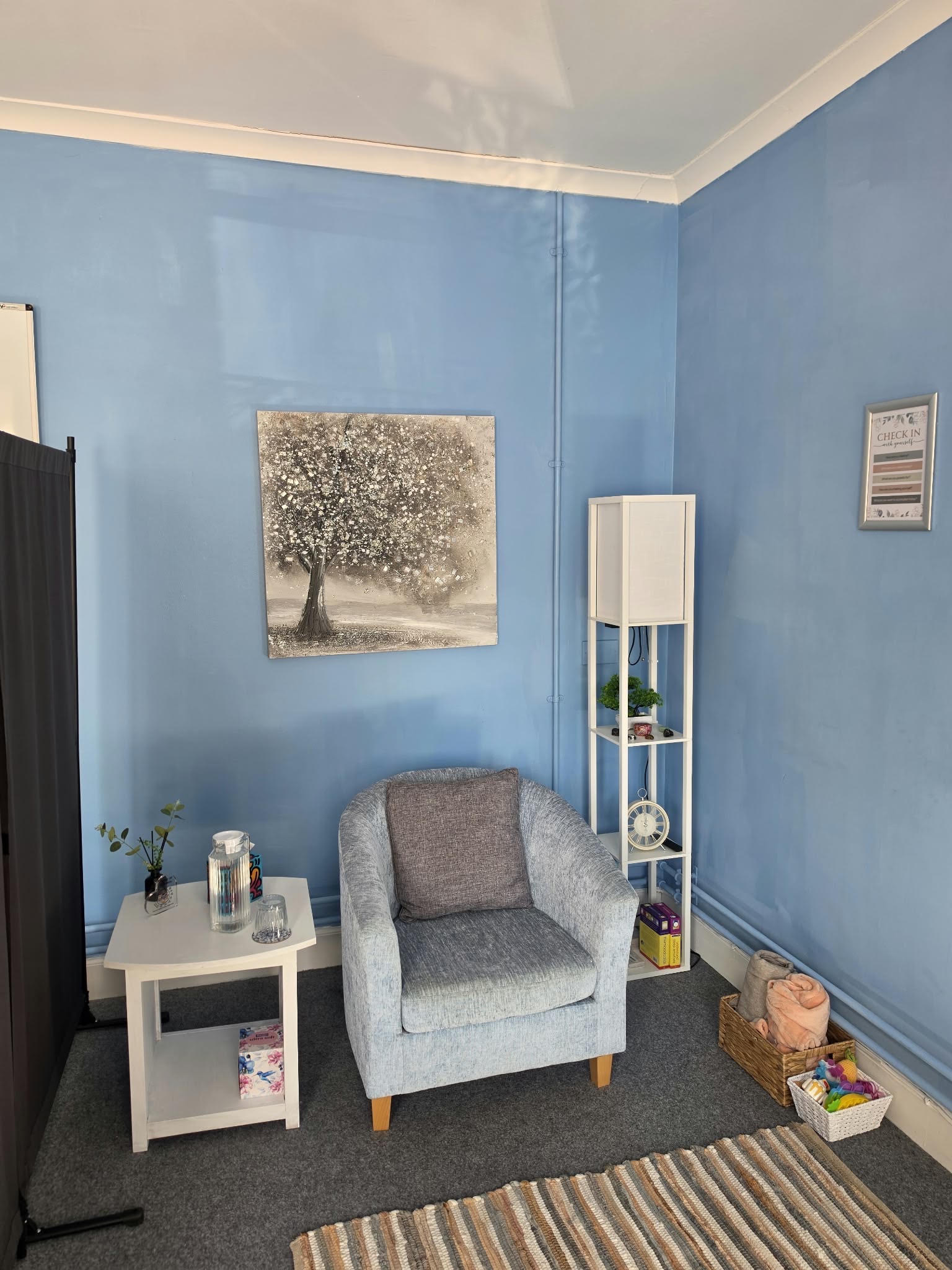 The counselling room, with a soft armchair beside a small table and a tree painting on the wall